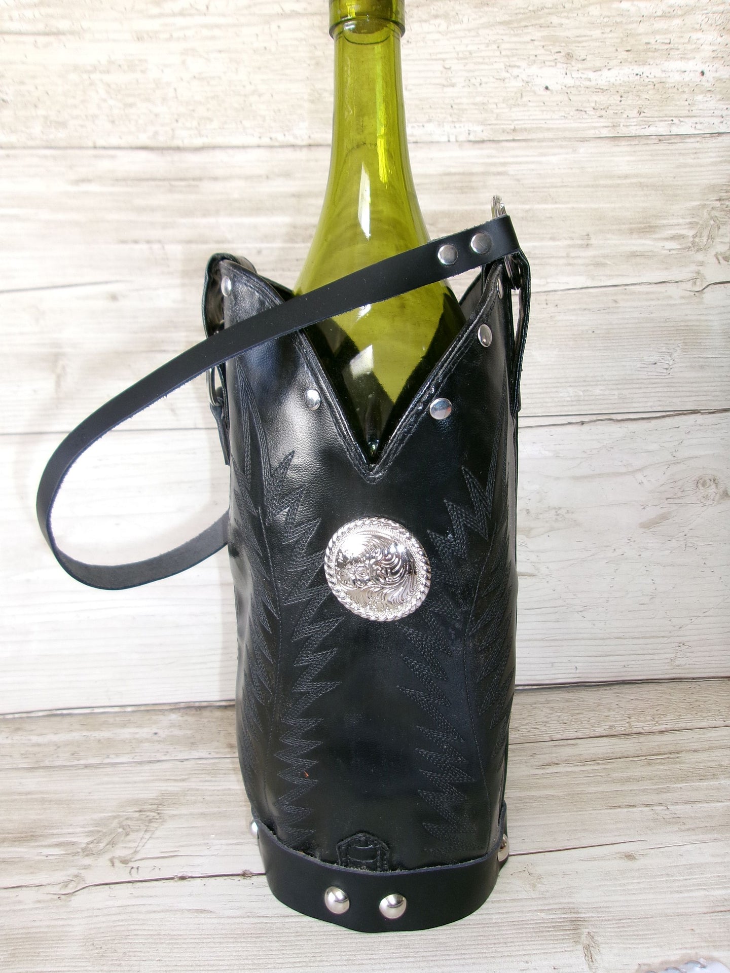 Black leather wine bottle holder with decorative concho on a wooden surface
