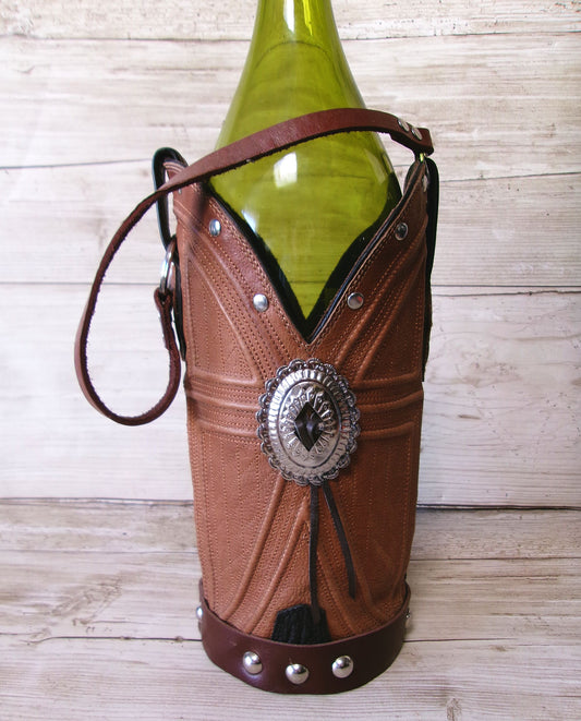 Brown leather wine bottle holder with decorative concho on a wooden surface