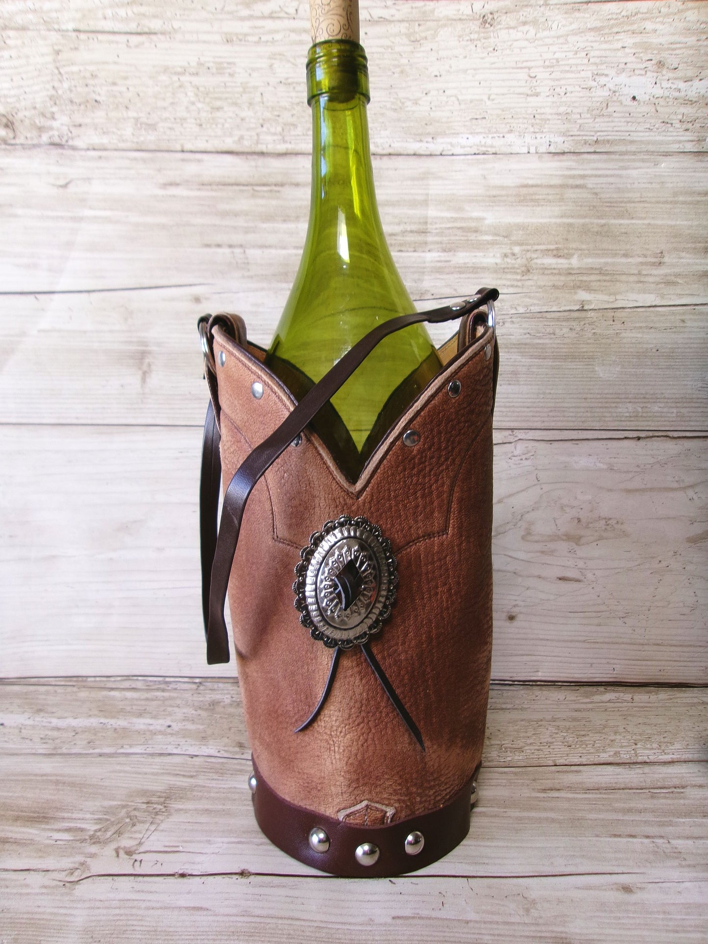 Wine bottle in a decorative leather holder with a concho on a wooden surface