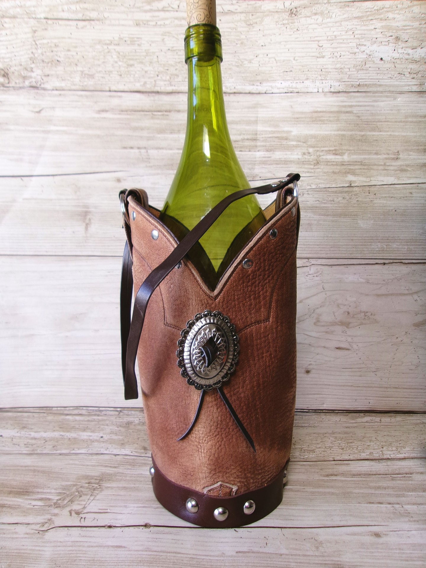 Wine bottle in a decorative leather holder with a concho on a wooden surface