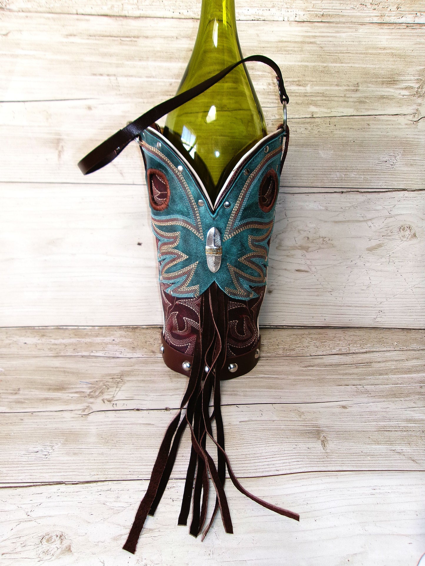 Decorative bottle holder shaped like a boot with a butterfly design, holding a green bottle on a wooden surface.