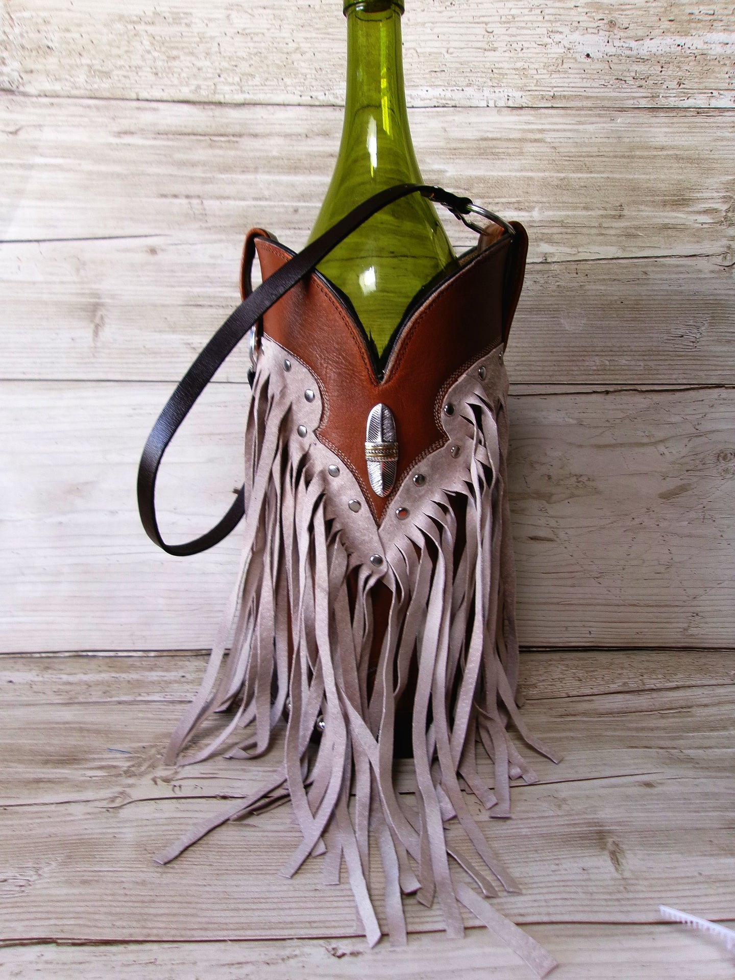Bottle holder with fringes and leather details on a wooden surface