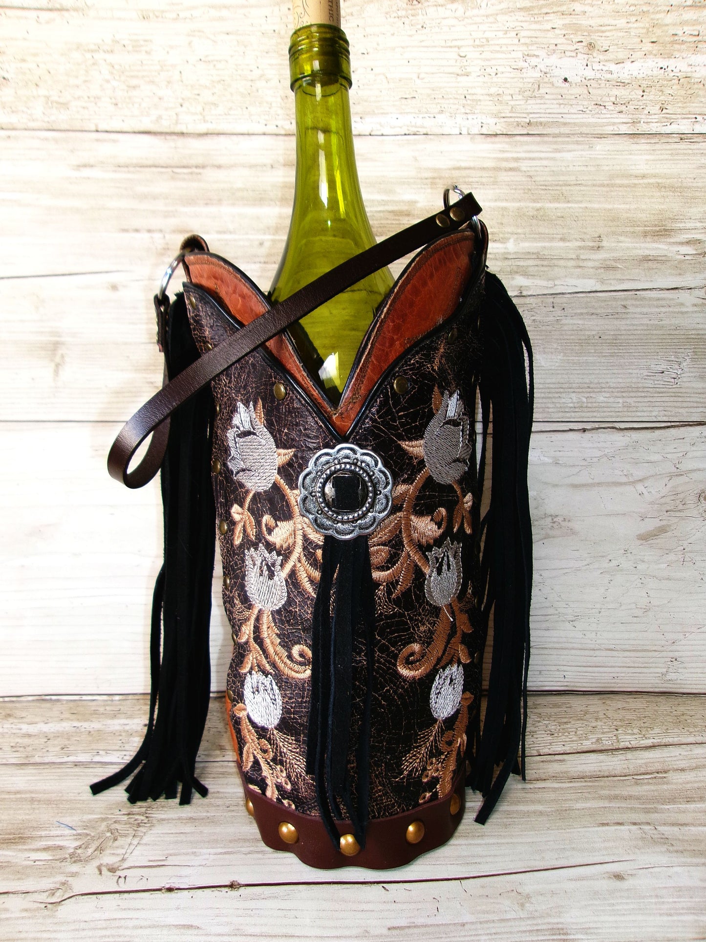 Decorative wine bottle holder with intricate designs and tassels on a wooden surface.